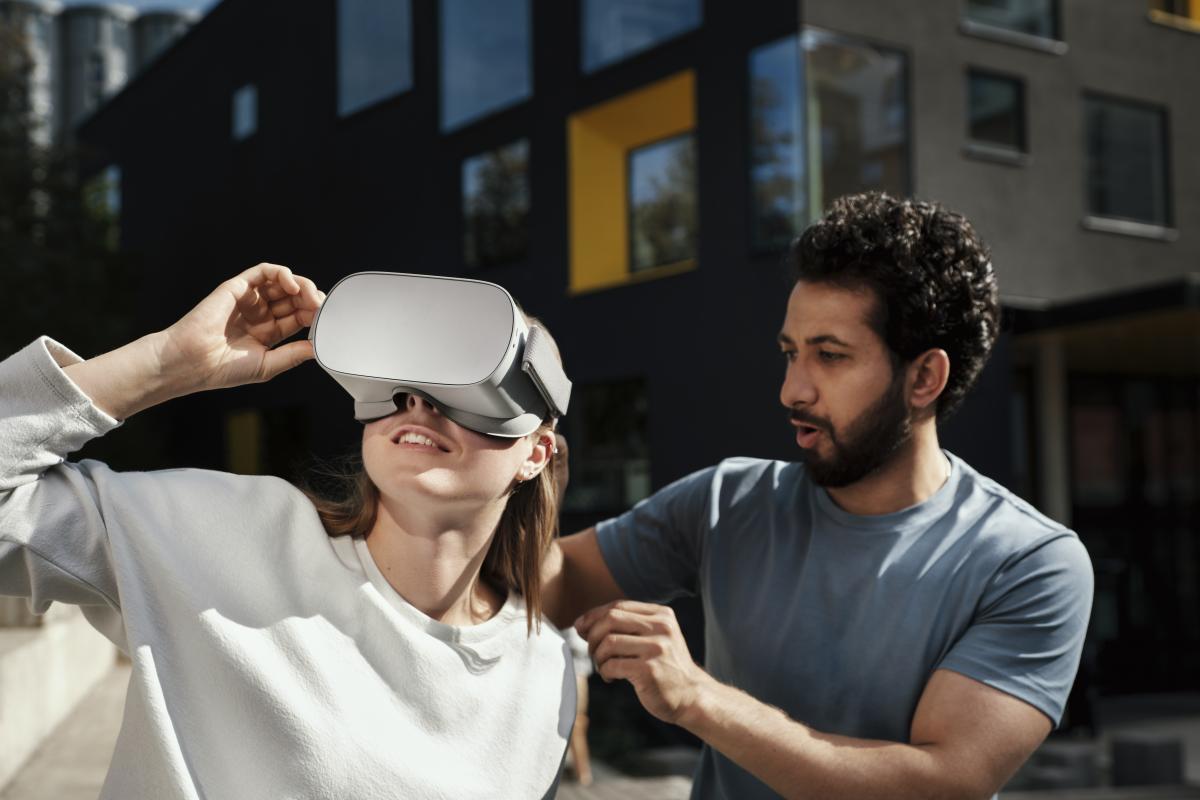 A woman wearing virtual reality headset and a man is helping her. 