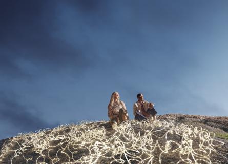 Expansive dark blue-sky backdrop, with a man and woman in the foreground surrounded by white LED rope lights.