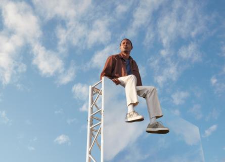 Expansive light blue-sky backdrop, with a man in the foreground sitting on top of large mirror