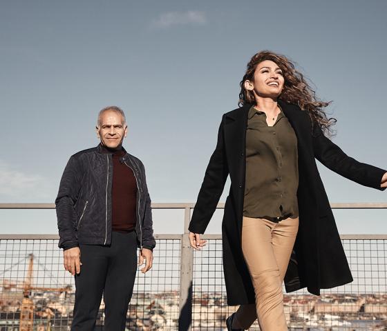 A man is standing on a rooftop and a woman is walking away from him.